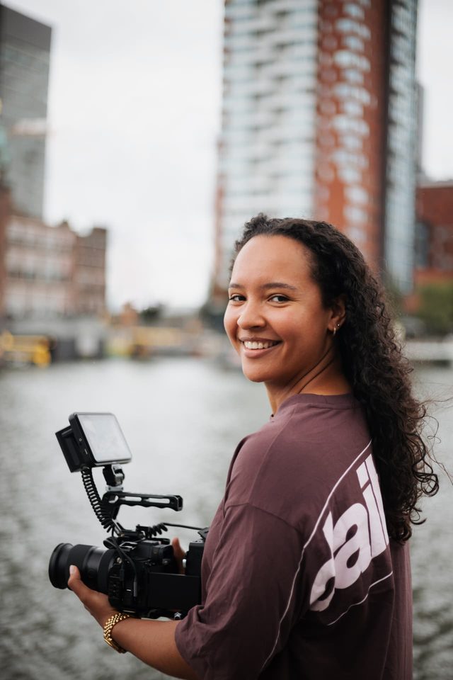Janelle met een filmcamera, kijkend over haar schouder